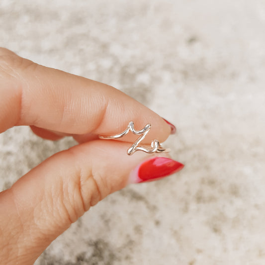 Handmade gold wire ring featuring a lowercase cursive letter Z, styled on a hand with elegant red french nails.