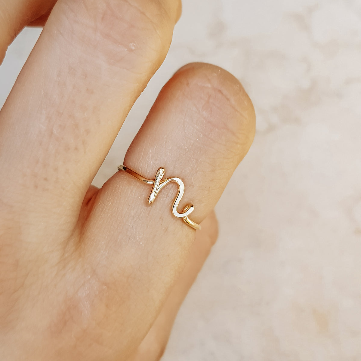 Close-up of a handmade 14k gold filled wire ring shaped into the letter N on a woman's finger.