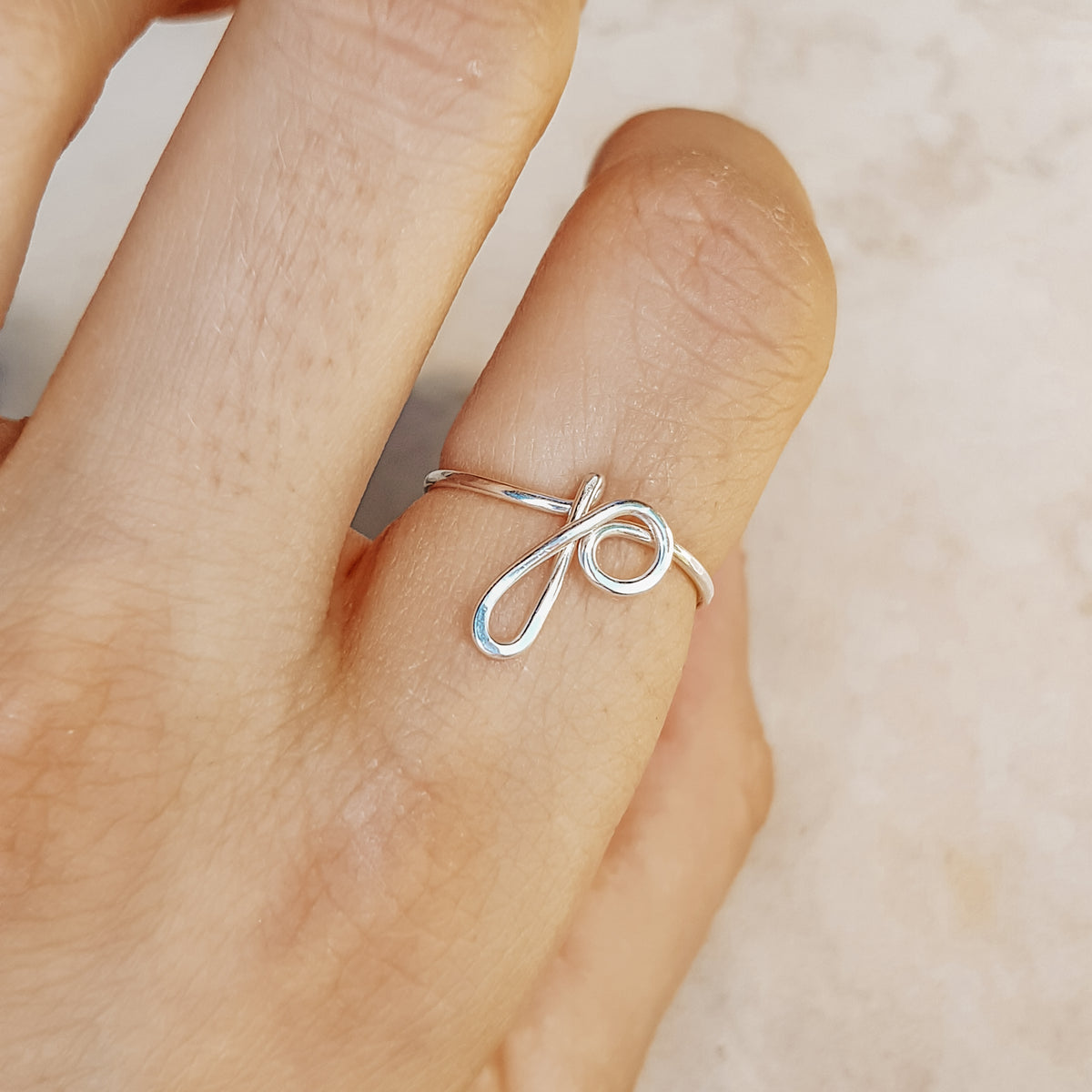 Close-up of a handmade 925 sterling silver wire ring shaped into the letter P on a woman's finger.