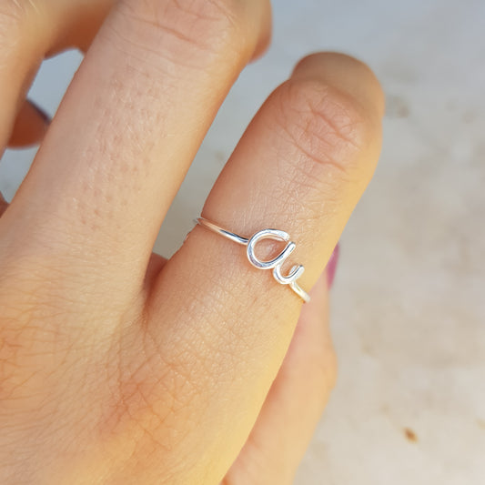 Close-up of a handmade 925 sterling silver wire ring shaped into the letter A on a woman's finger.
