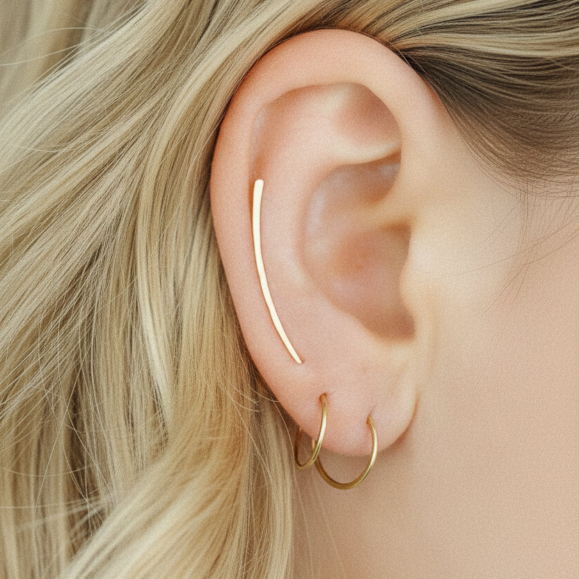 Minimal thin gold wire hoop earrings worn on the ear with layered lobe styling