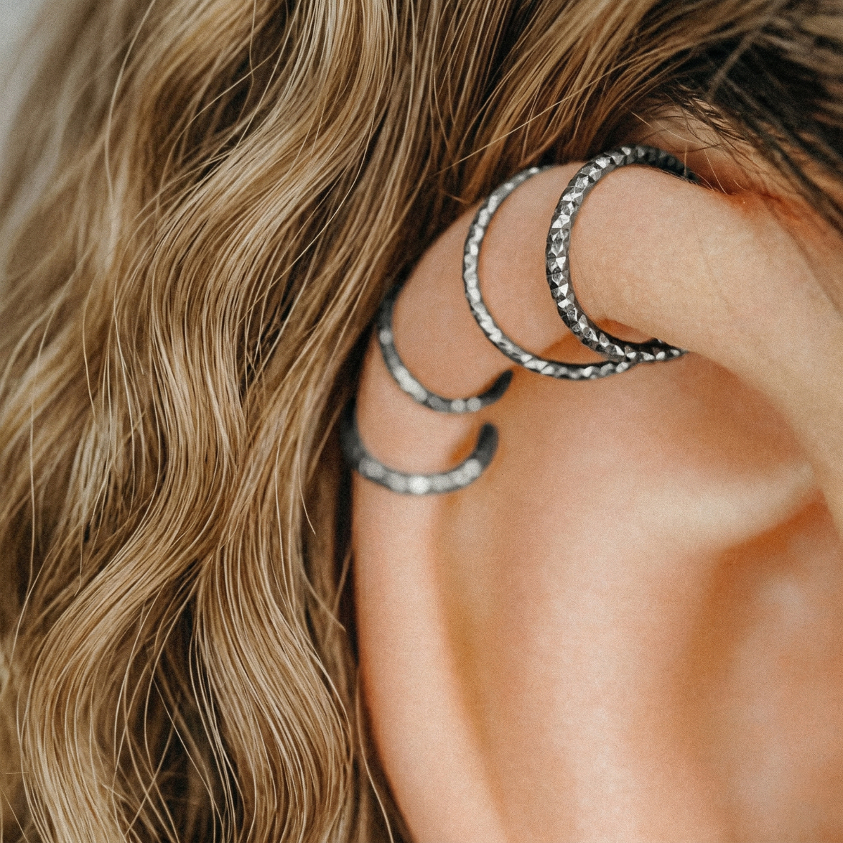 Close-up of a model wearing multiple black diamond-cut hoops in a helix piercing.