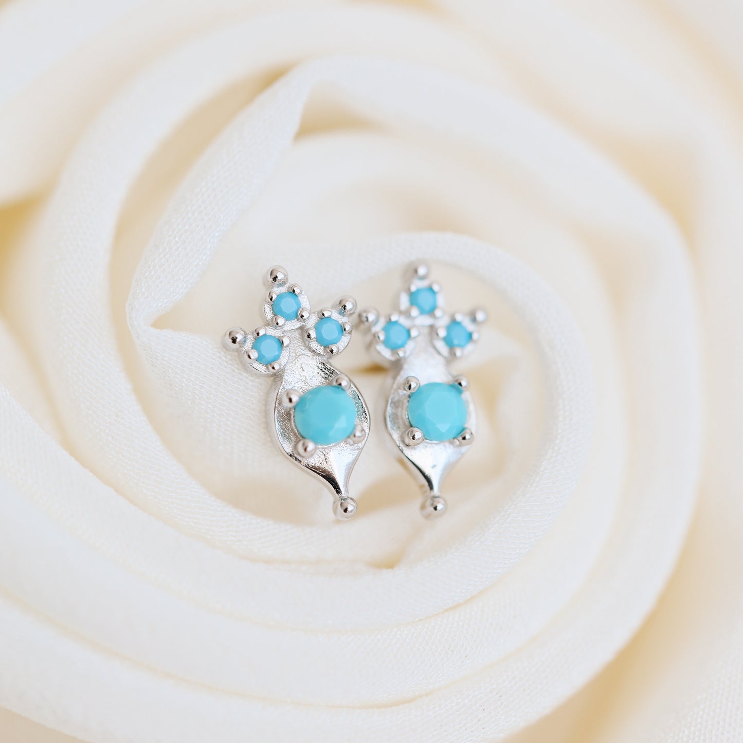 Dainty turquoise earrings on white fabric background