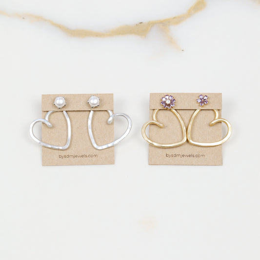 Handmade open heart Ear Jacket earrings designed to sit behind the pierced earlobe beneath an interchangeable stud, available as one Ear Jacket or a matching pair in gold or silver hammered aluminum, approximately 25 mm in diameter, with one coordinating pair of stainless steel post stud earrings included with each order; stud designs vary according to current availability and those shown in the photos are styling examples rather than guaranteed designs.