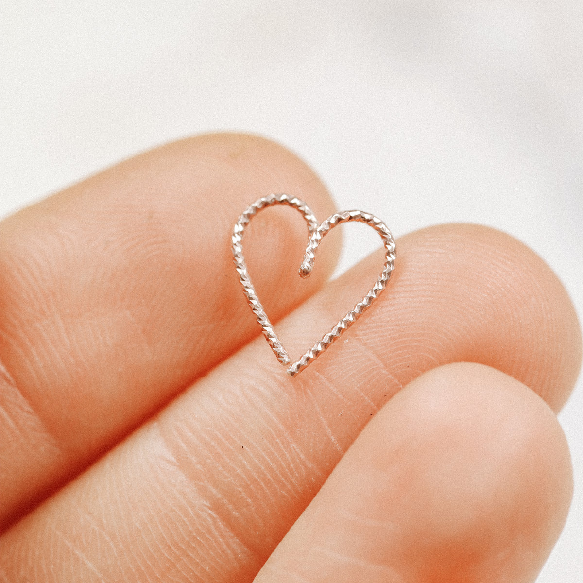 Close-up of a diamond-cut heart-shaped hoop earring in 18k rose gold plating on a white marble background, showing the sparkling textured finish.
