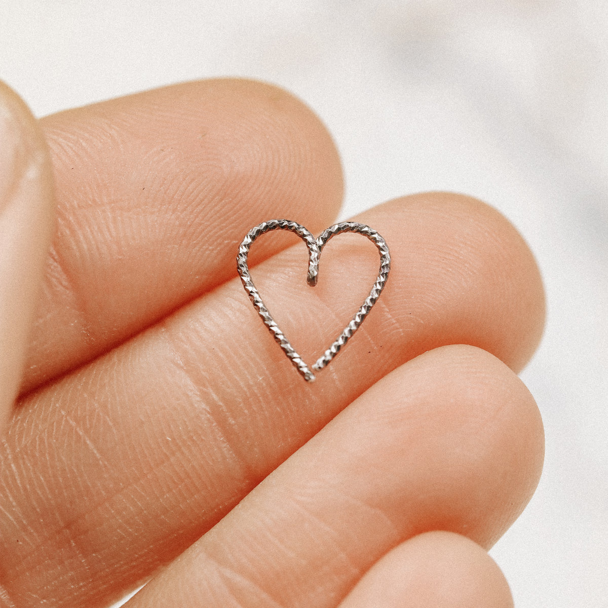 Detailed view of the open bend-and-twist mechanism of a black heart-shaped cartilage hoop for helix and daith piercings.
