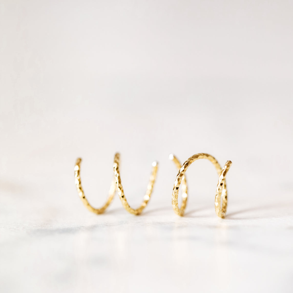 Minimal gold double hoop earrings with spiral twist design worn on ear, illusion of double piercing, diamond cut sterling silver jewelry