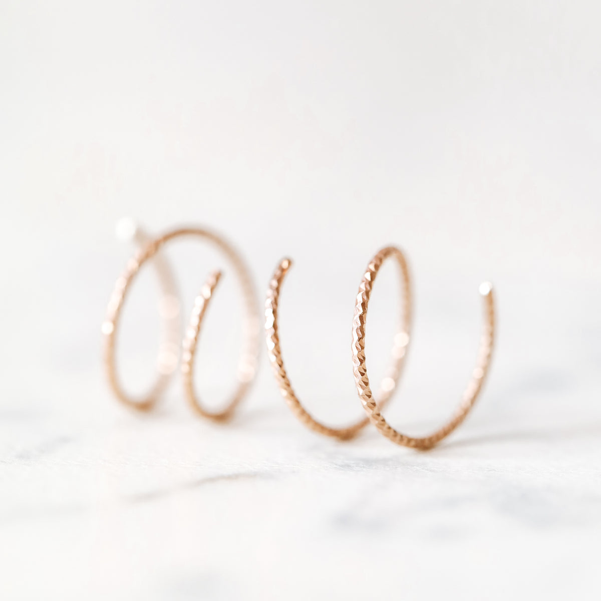 Close-up of a woman's ear wearing tiny rose gold double hoop illusion earrings with a diamond-cut texture, designed to create the appearance of two piercings with a single hole.