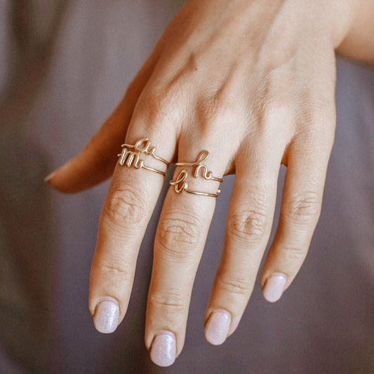 Close-up of a handmade 14k gold filled wire ring shaped into the letter A, M, H and L on a woman's finger.