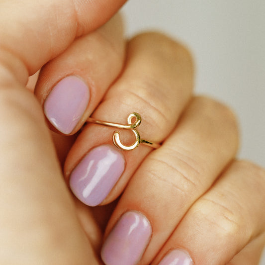 Close-up of a handmade 14k gold filled wire ring shaped into the letter S on a woman's finger.