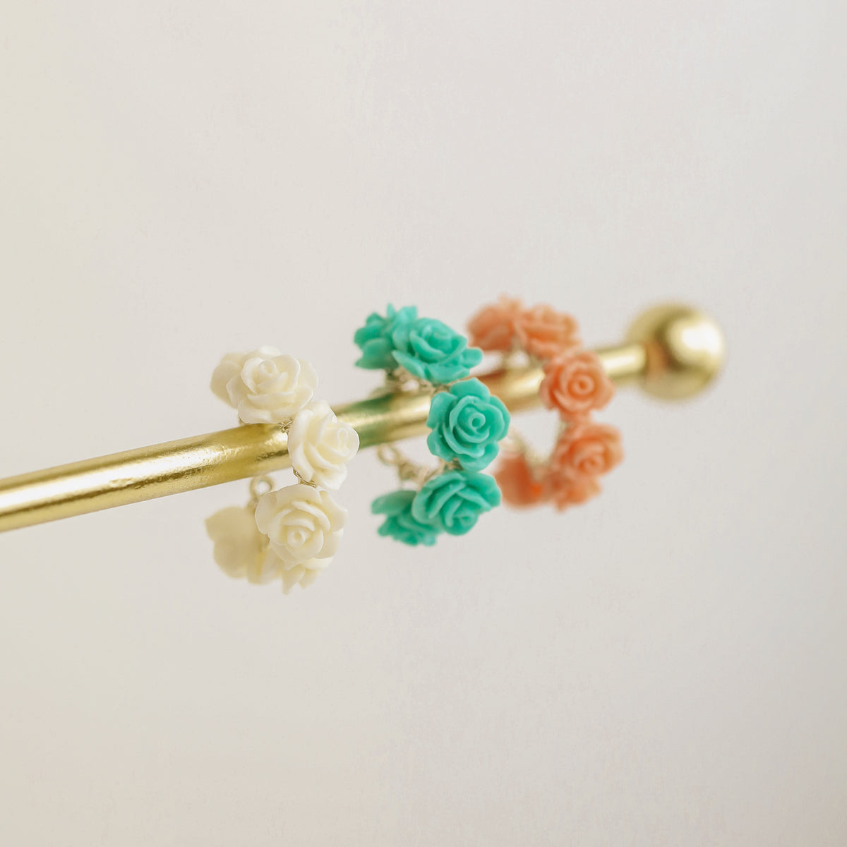 Floral resin rose conch ear cuffs displayed on a gold jewelry stand in white ivory, turquoise aqua blue and peach coral colors