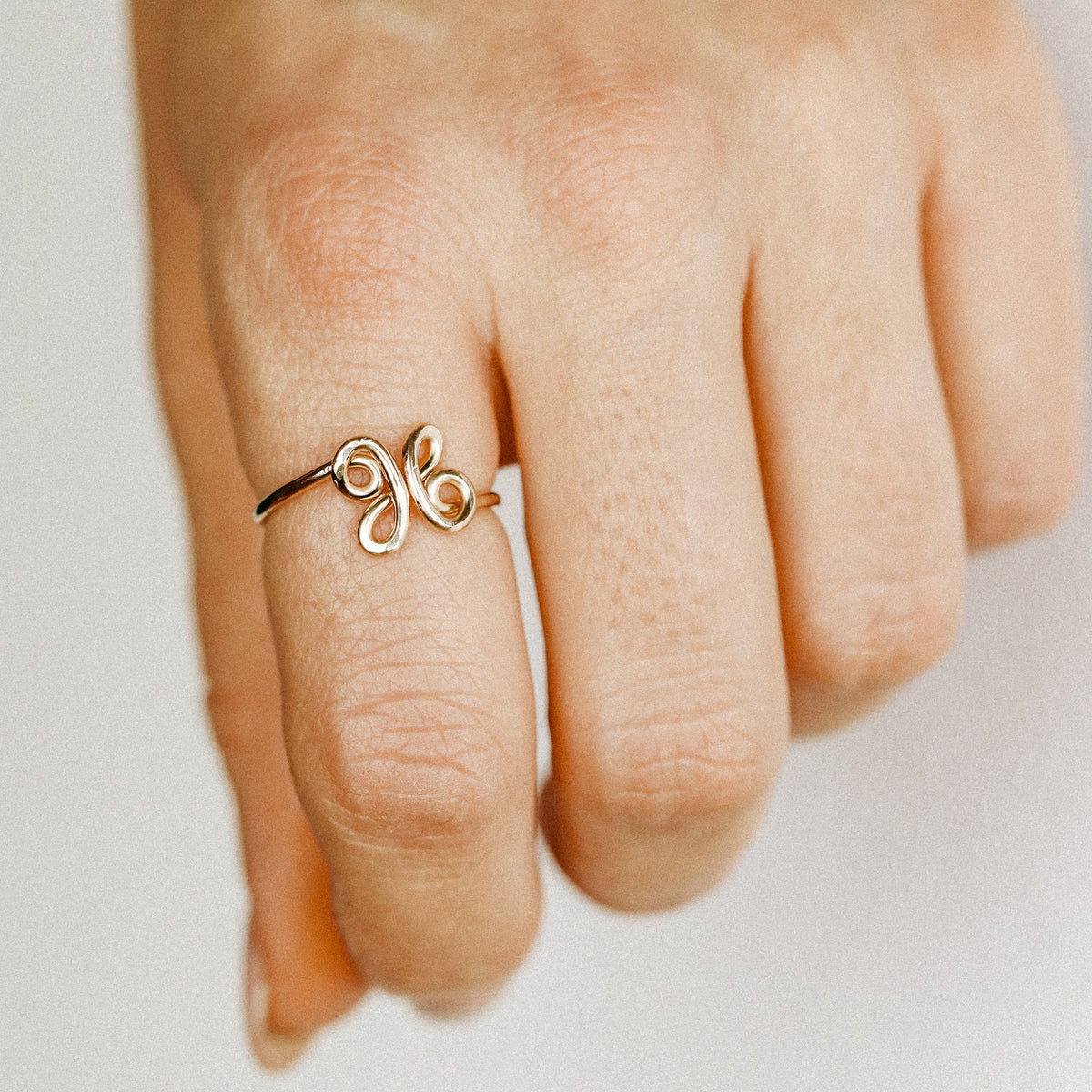 Close-up of a handmade 14k gold filled wire ring shaped into the letter X on a woman's finger.