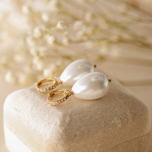 Pair of 18k gold-plated huggie hoop earrings with premium teardrop pearl drops and cubic zirconia crystals, displayed on a beige velvet jewelry box.