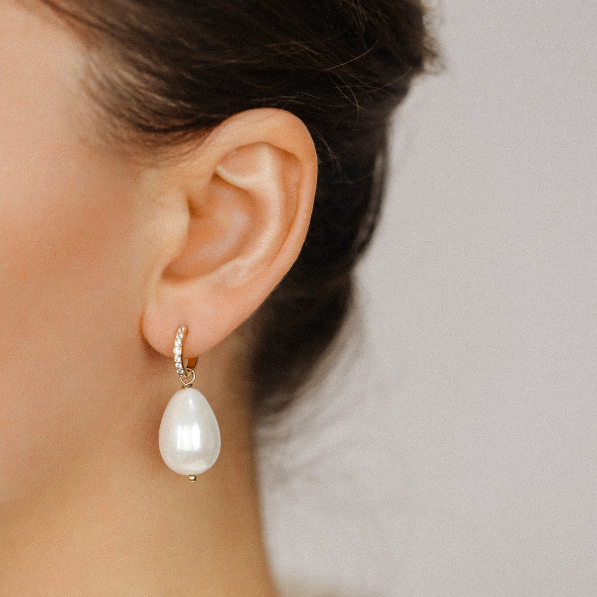 Lifestyle image of a woman wearing a gold-plated stainless steel hoop earring with a large lustrous artificial teardrop pearl for wedding or formal wear.