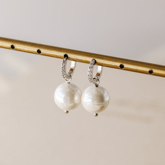Pair of handmade ceramic pearl earrings hanging on a gold jewelry display stand.