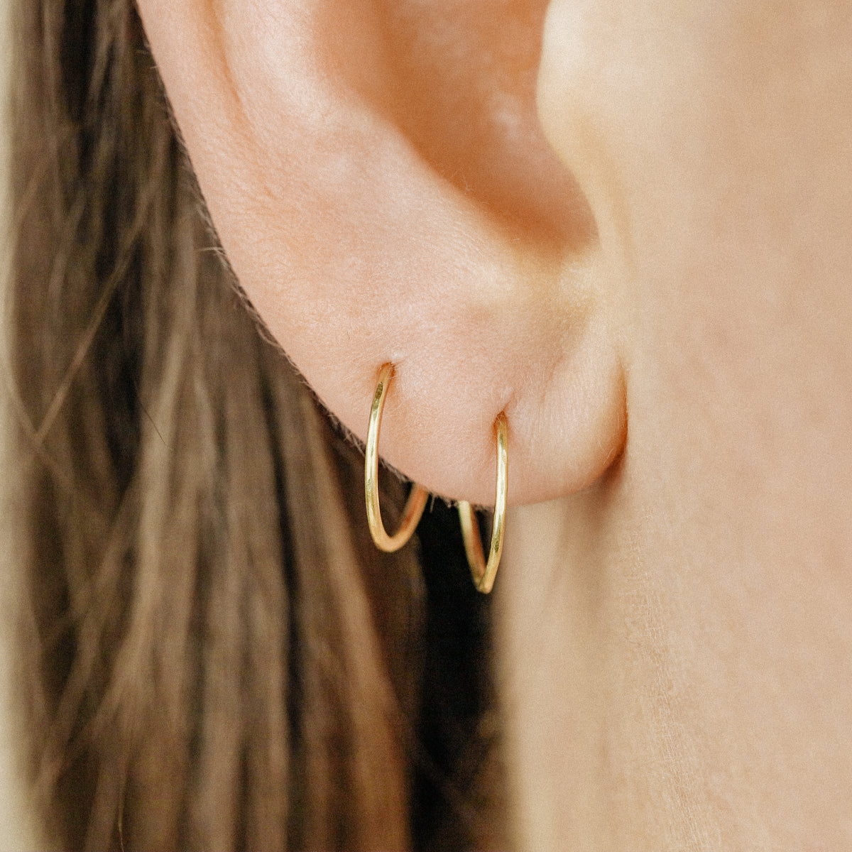 Minimal thin gold wire hoop earrings worn on the ear with layered lobe styling