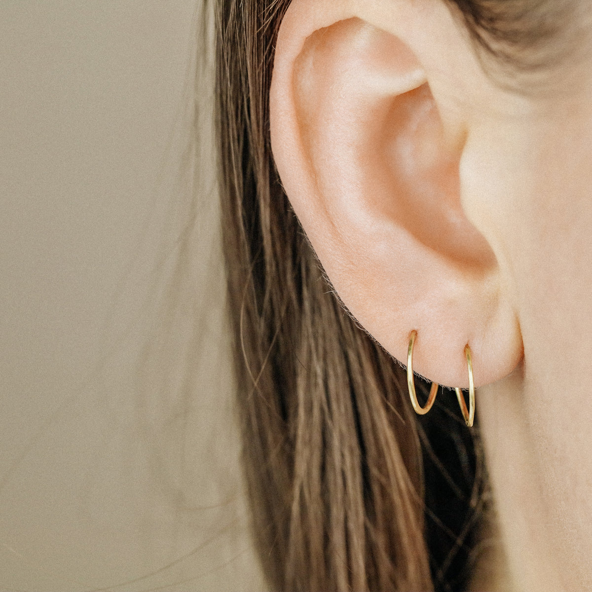 Close-up of minimal round gold wire hoop earrings worn on the ear
