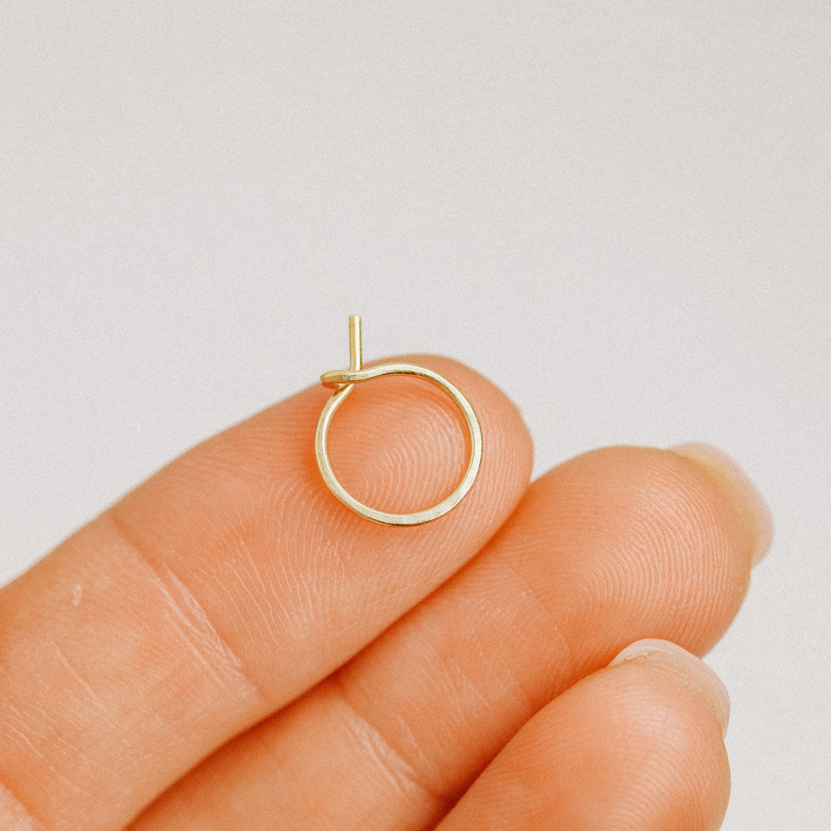 Single small gold wire hoop earring held on fingertips to show size and shape