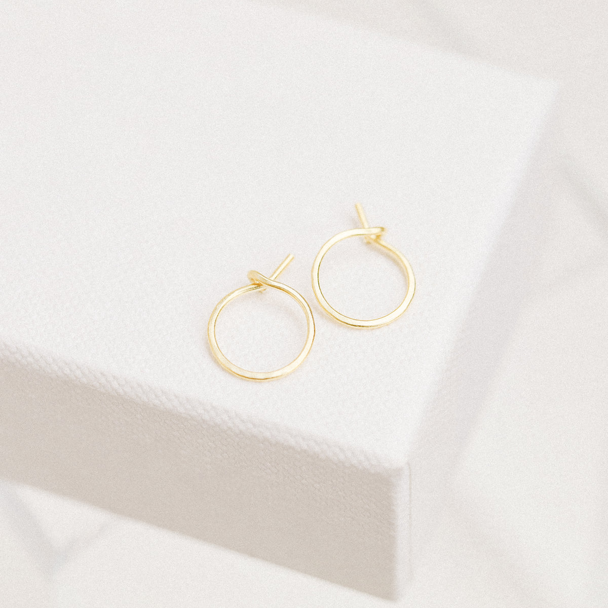 Minimal thin gold wire hoop earrings displayed on soft white fabric