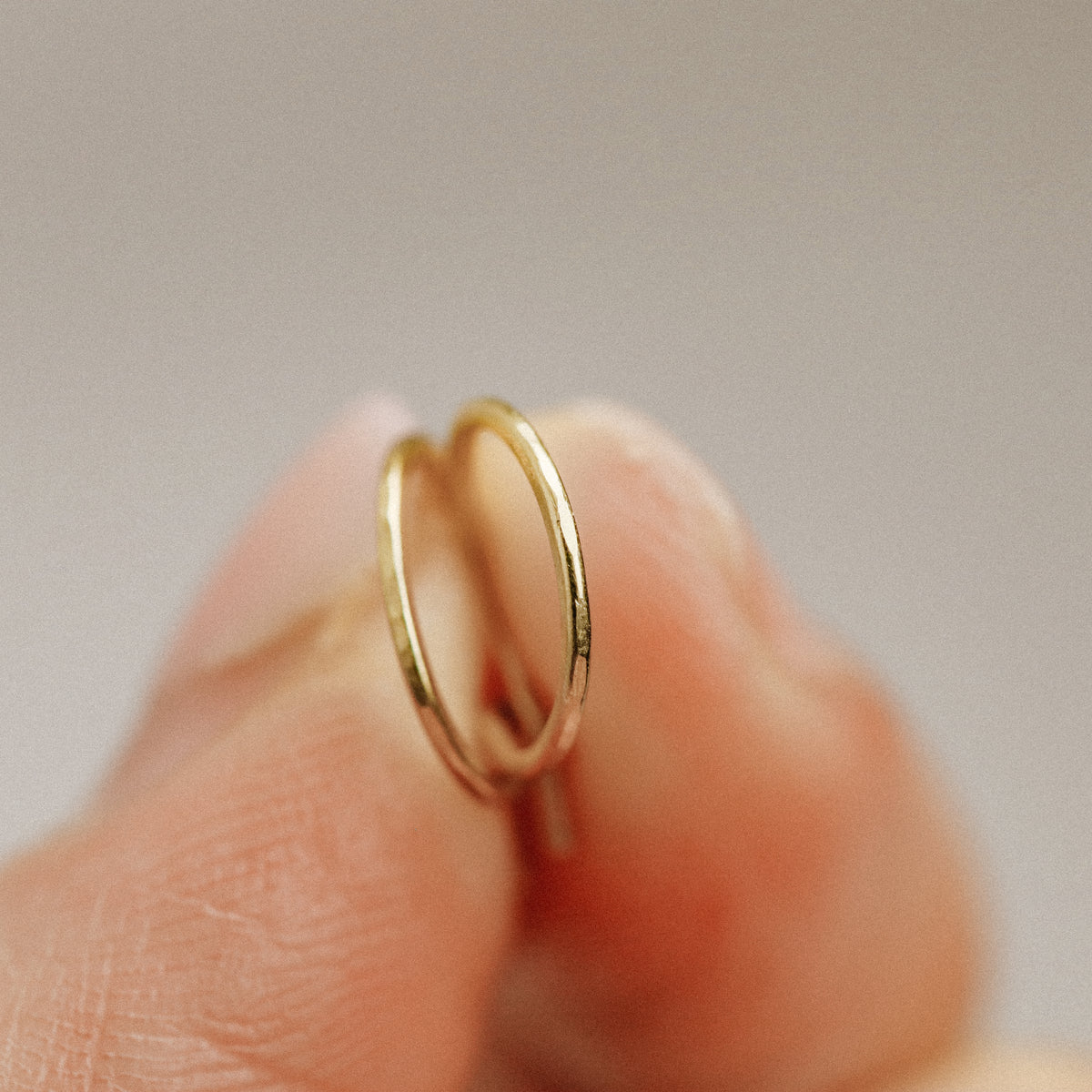 Single small gold wire hoop earring held on fingertips to show size and shape