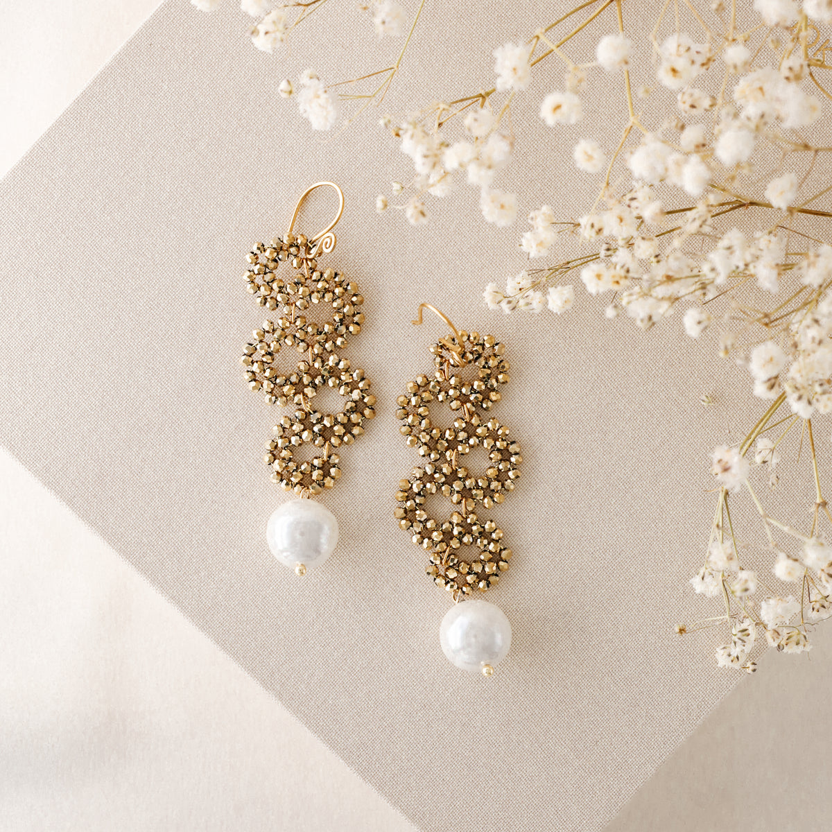 Gold crystal cascading earrings with pearl drop on neutral fabric background