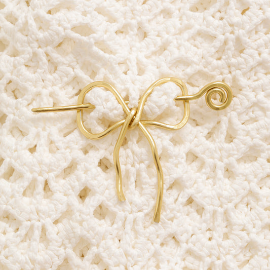 Handmade aluminum bow shawl pin brooch with matching removable stick pin, shown in gold and available in silver or gold finish, designed as a decorative and functional scarf fastener for shawls, sweaters, cardigans, knit wraps and crochet pieces, with a romantic bow shape and minimalist metal design.