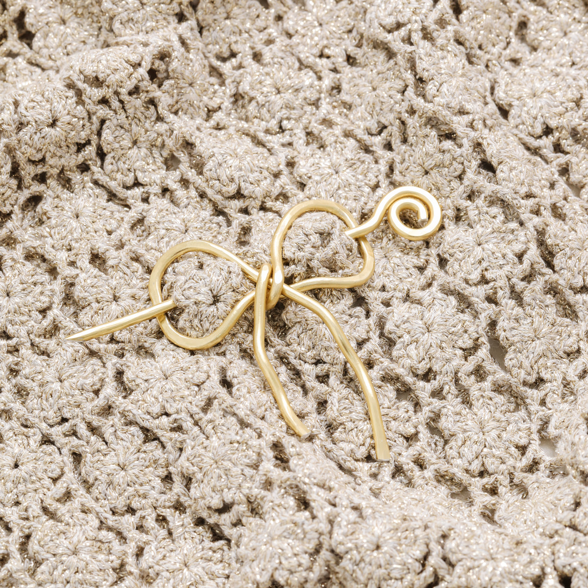 Handmade aluminum bow shawl pin brooch with matching removable stick pin, shown in gold and available in silver or gold finish, designed as a decorative and functional scarf fastener for shawls, sweaters, cardigans, knit wraps and crochet pieces, with a romantic bow shape and minimalist metal design.