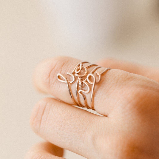Close-up of a handmade 14k rose gold filled wire ring shaped into the letter L, O, V and E on a woman's finger.