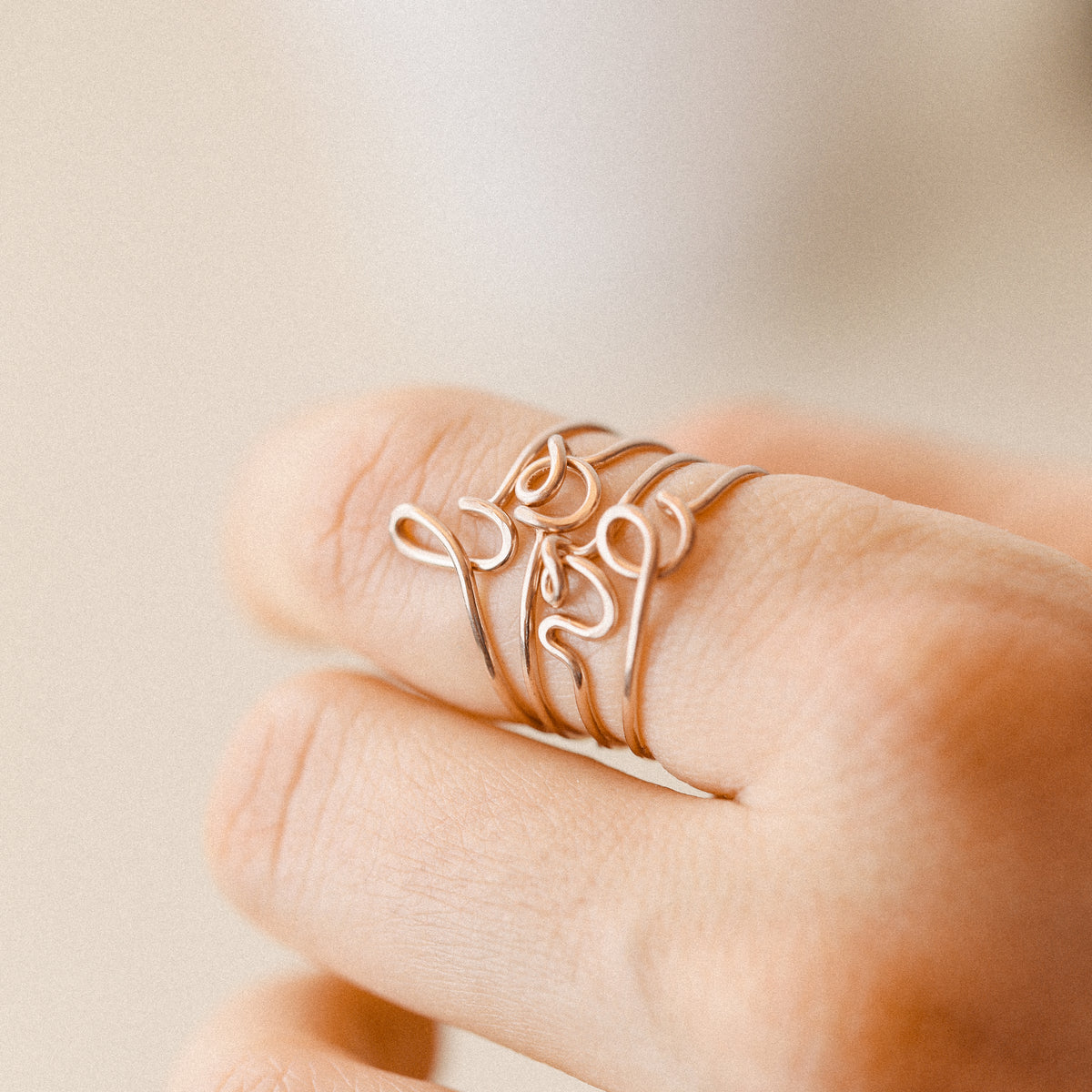 Close-up of a handmade 14k rose gold filled wire ring shaped into the letter L, O, V and E on a woman's finger.