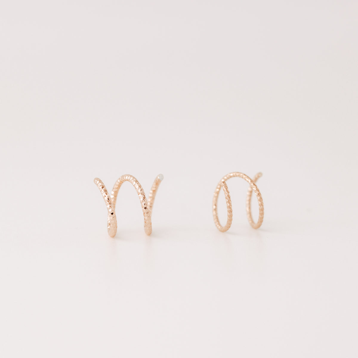 Close-up of a woman's ear wearing tiny rose gold double hoop illusion earrings with a diamond-cut texture, designed to create the appearance of two piercings with a single hole.