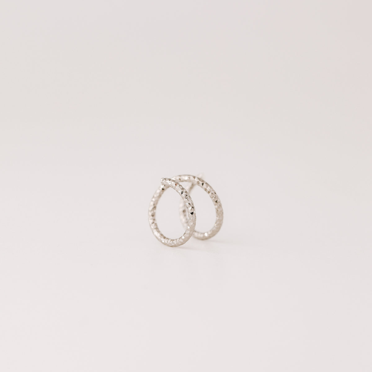 Minimal black double hoop spiral earrings worn on ear, tiny ruthenium sterling silver illusion hoops creating double piercing look, diamond cut texture close-up