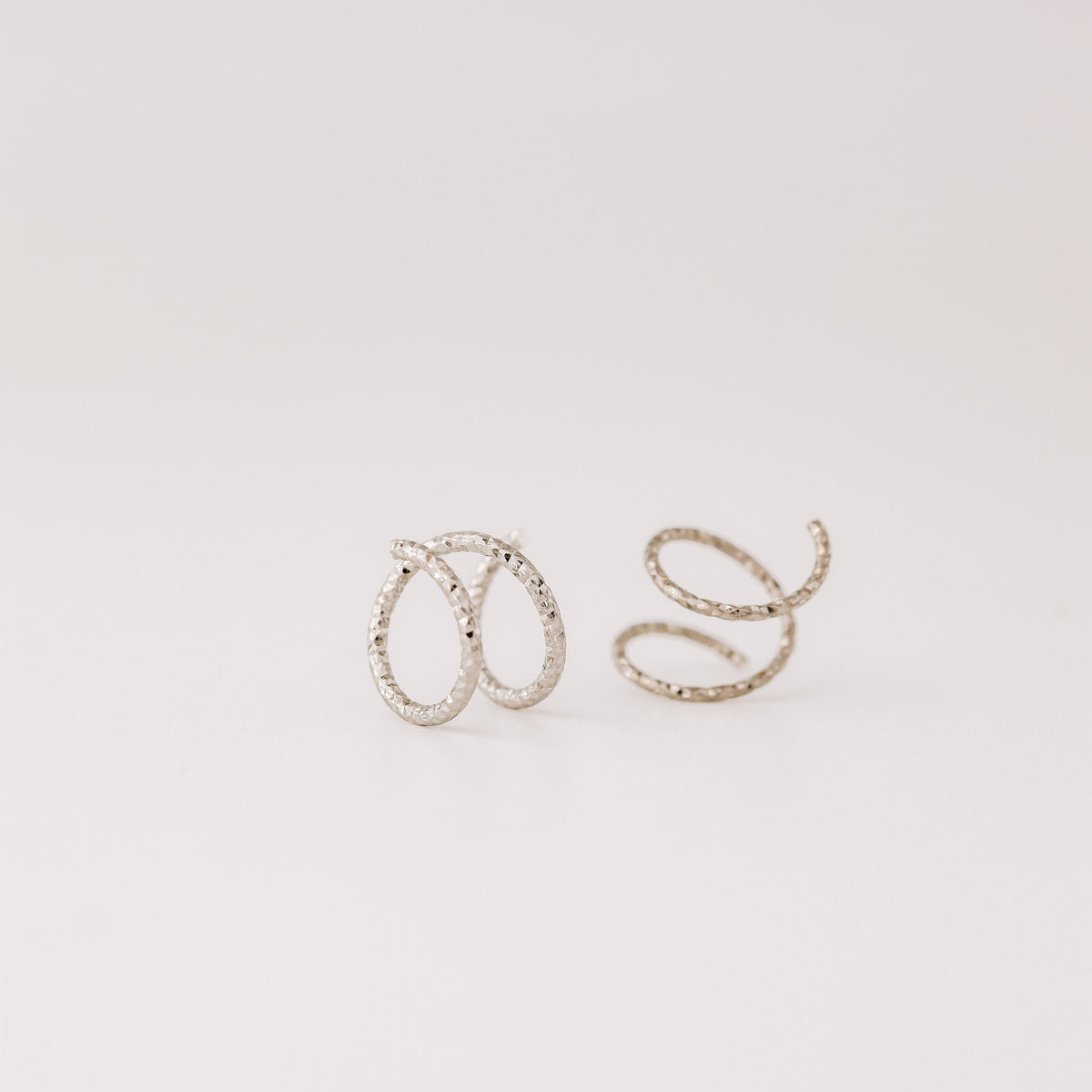 Minimal black double hoop spiral earrings worn on ear, tiny ruthenium sterling silver illusion hoops creating double piercing look, diamond cut texture close-up