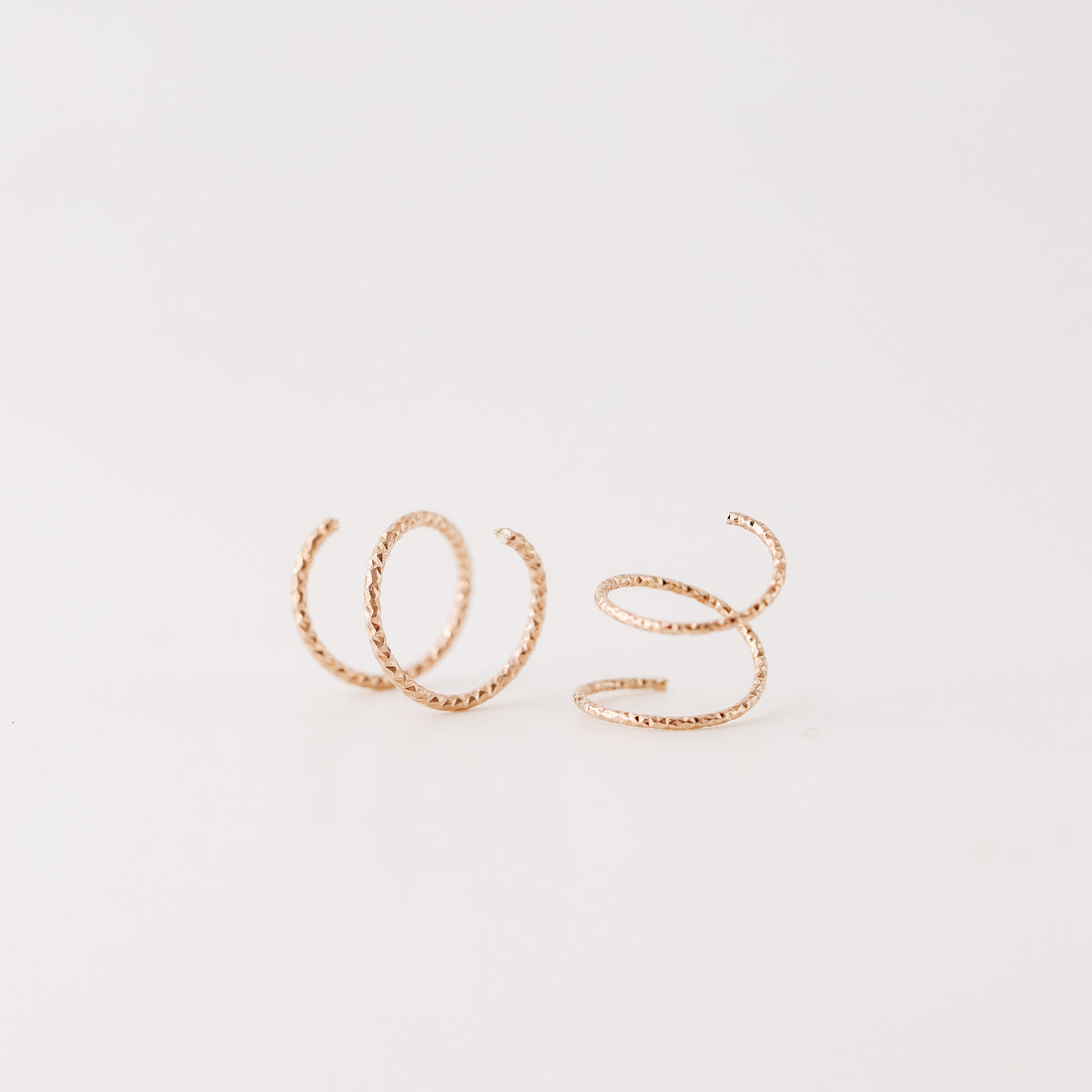 Close-up of a woman's ear wearing tiny rose gold double hoop illusion earrings with a diamond-cut texture, designed to create the appearance of two piercings with a single hole.