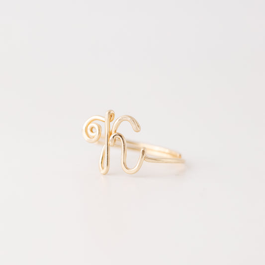 Handmade uppercase cursive letter K wire ring in polished gold, shown from a side view on a clean white background.