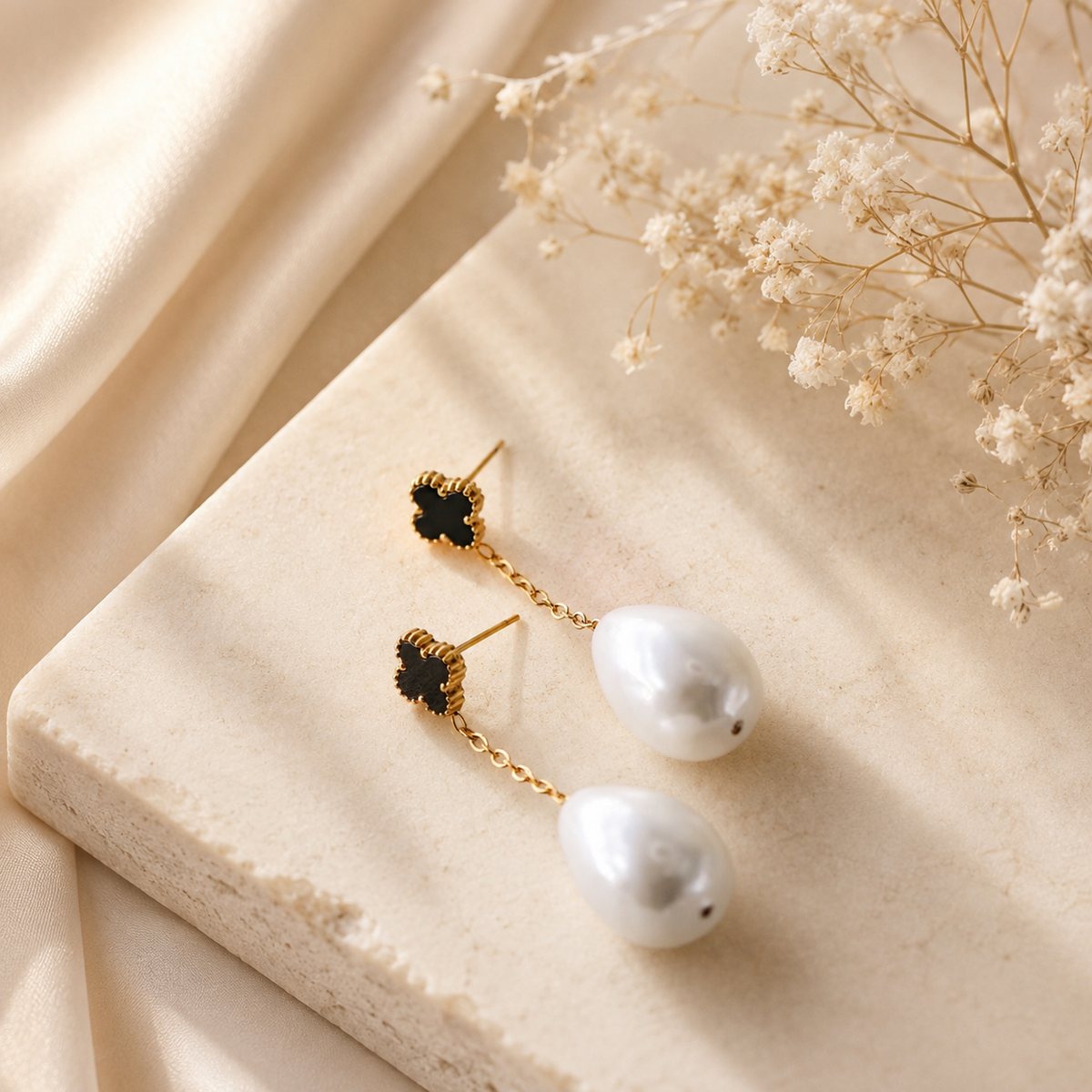 Black clover pearl drop earrings displayed on neutral fabric with gold chain detail