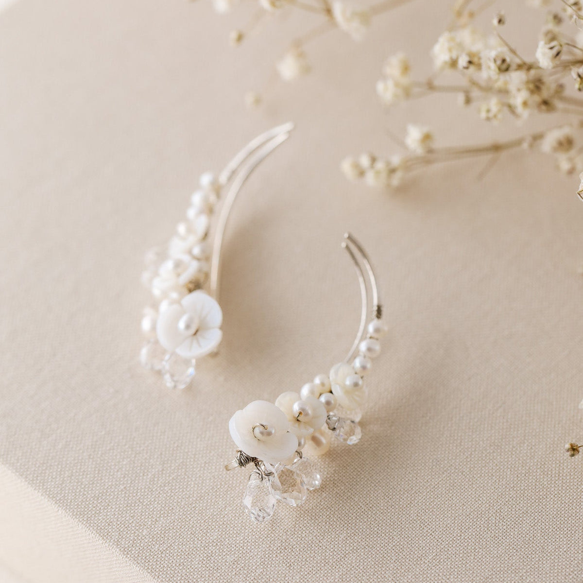 Floral crystal ear climbers held between fingers for size reference