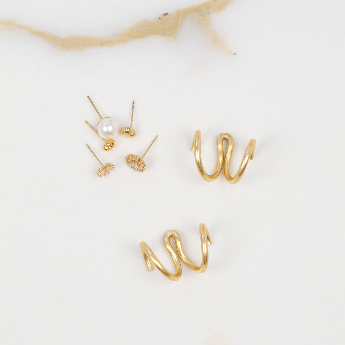 Two gold handmade double loop Ear Jacket backs displayed separately with assorted stud earrings, highlighting the flowing hand-shaped curves.