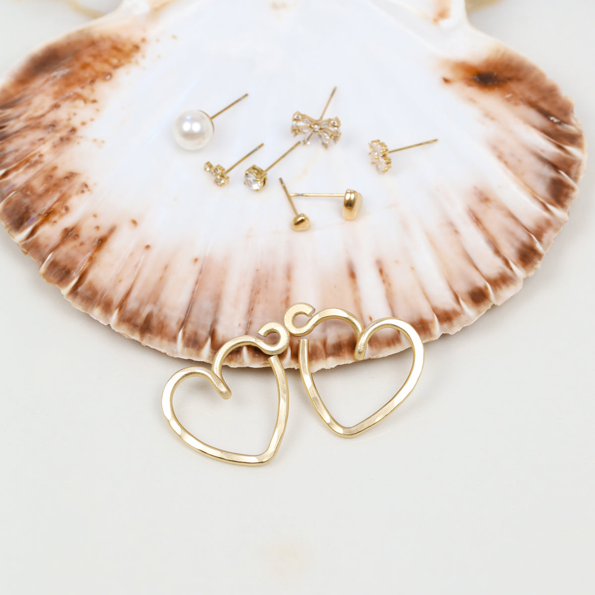 Close-up of two gold hammered aluminum Heart Ear Jackets showing the open heart silhouette, textured handmade surface and small curved top detail.