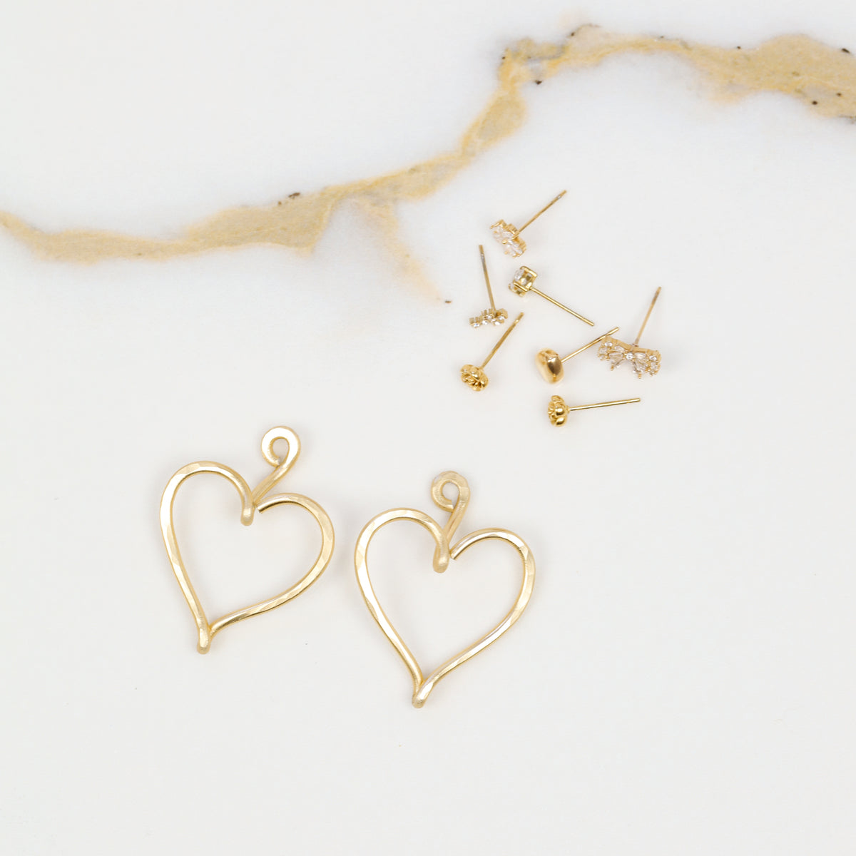 Close-up of a pair of handmade gold Large Heart Ear Jackets, showing the open elongated heart shape, hammered surface and curved top detail.