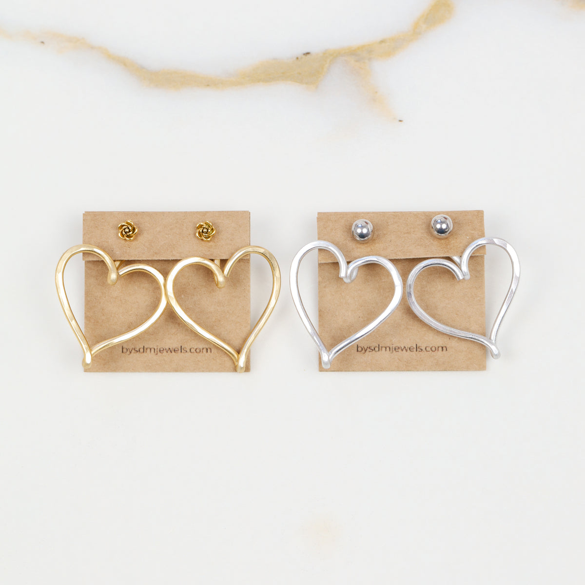 Gold and silver Large Heart Ear Jacket pairs displayed side by side with example stud earrings, showing both available colors and the handmade open heart design.