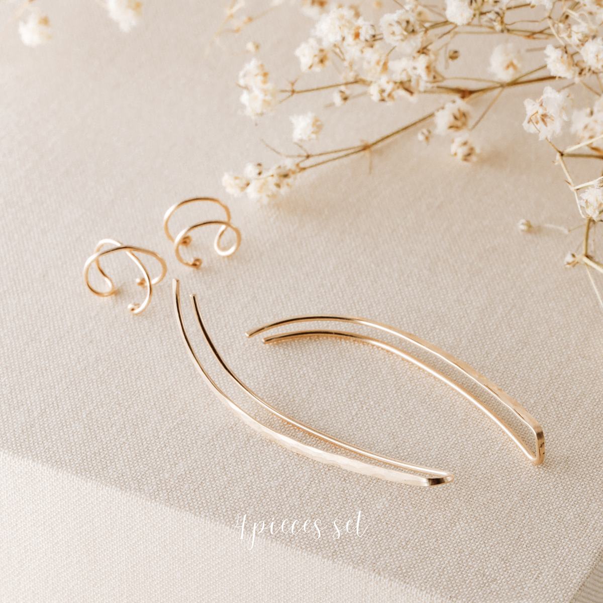 4 pieces ear climber set displayed on beige fabric with dried white flowers, featuring a pair of long hammered ear climbers, one Double Line no-piercing helix cuff and one Criss-Cross no-piercing helix cuff in a warm gold finish.