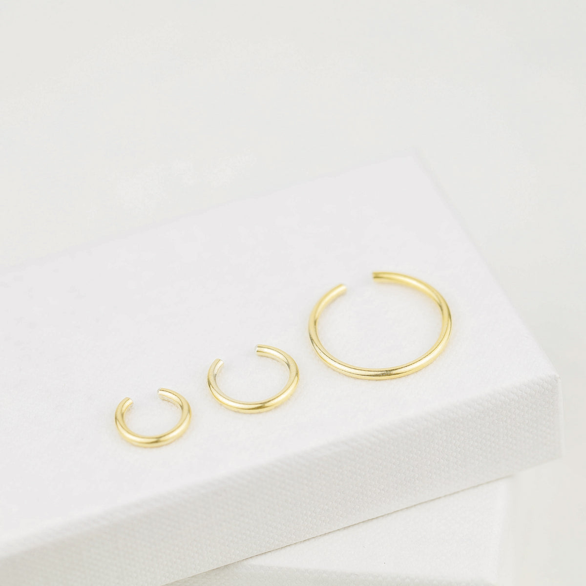 Thick smooth no-piercing ear cuff shown worn on different areas of the ear, including lobe, conch, cartilage and upper helix, with a rounded wrap design available in sterling silver, 18k yellow gold plated sterling silver, 18k rose gold plated sterling silver and black aluminum.