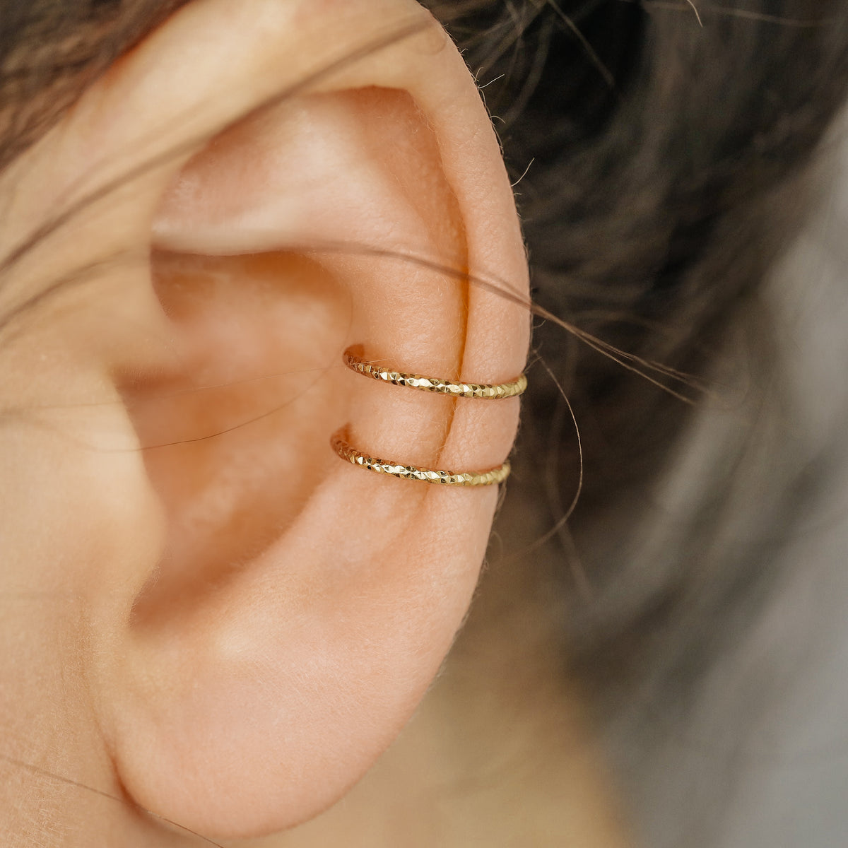 Gold double band ear cuff worn on the upper ear, featuring a slim no piercing design with diamond cut sparkle texture.