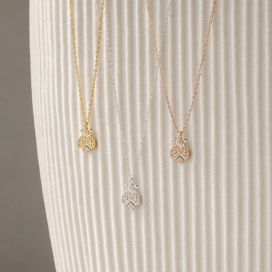 Ladybug necklaces displayed in silver gold and rose gold finishes on neutral ribbed background