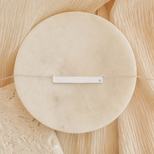 Sterling silver bar necklace photographed flat on round neutral stone surface