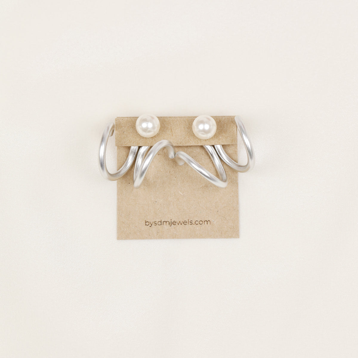 Pair of silver wavy double loop Ear Jackets displayed with pearl-style stud earrings, showing the matching pair configuration and flowing curved shape.