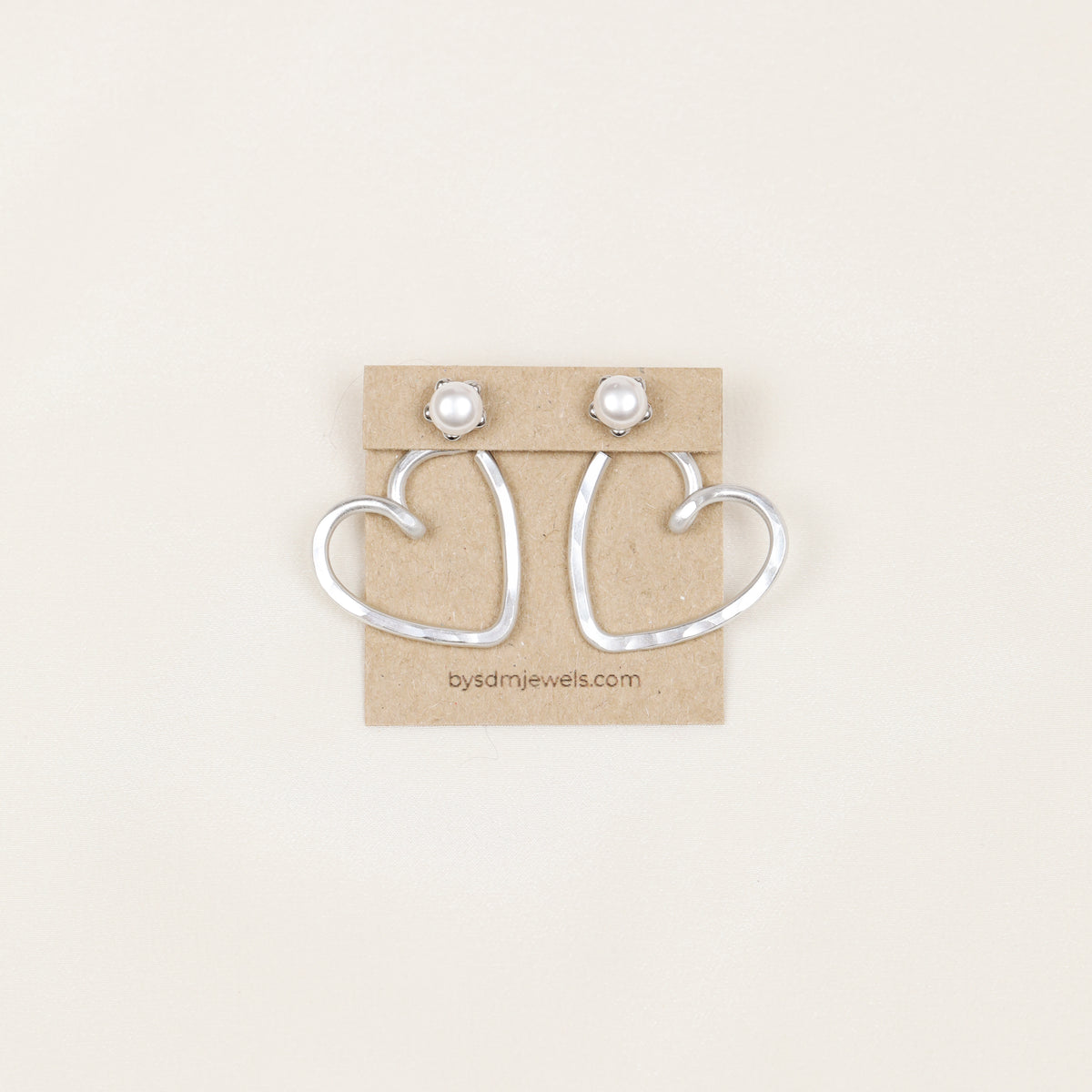 Pair of handmade silver aluminum Heart Ear Jackets displayed on a jewelry card with pearl-style stud earrings, showing the open hammered heart shape.