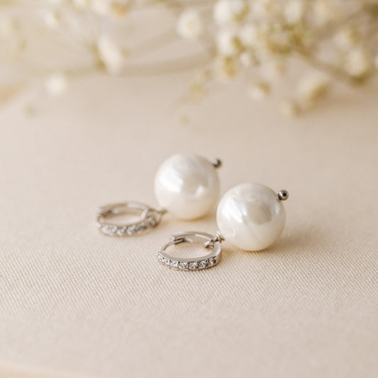 Silver pearl drop hoop earrings styled on neutral fabric with soft floral background