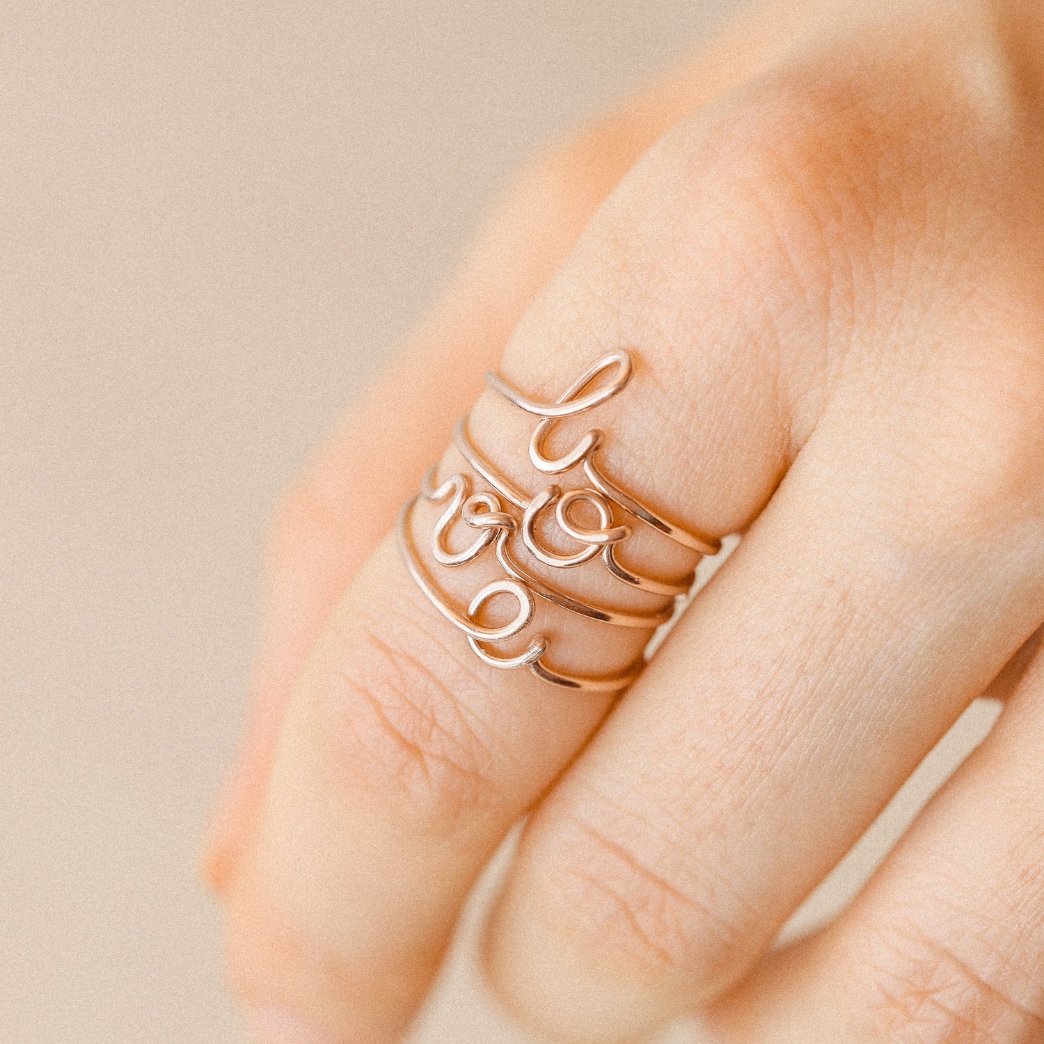 Stack of handmade cursive initial rings in rose gold on a model's hand.