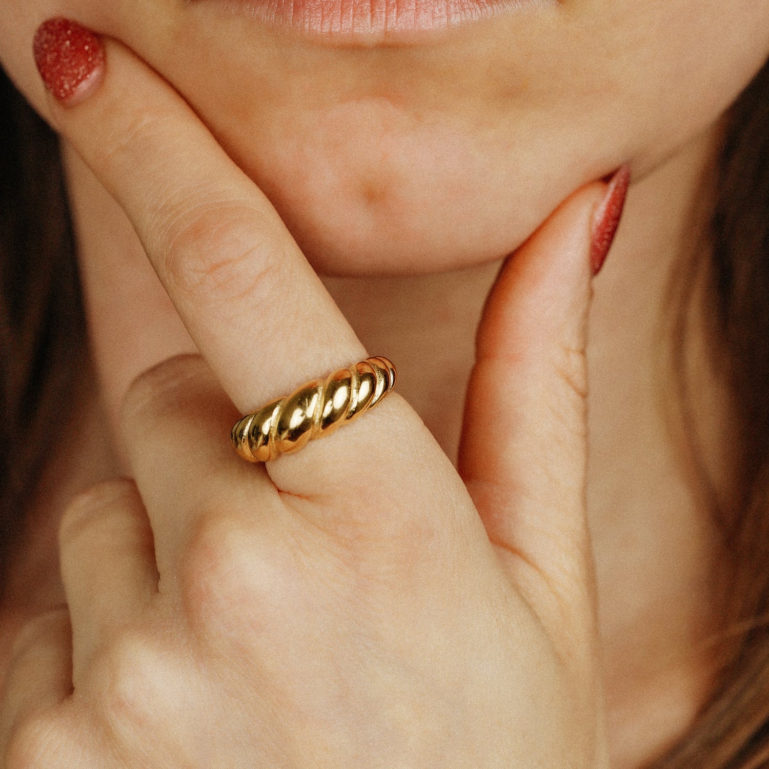 Close-up of a model's hand wearing the bold gold Croissant Ring, featuring a chunky twisted texture, styled with red glitter nails.